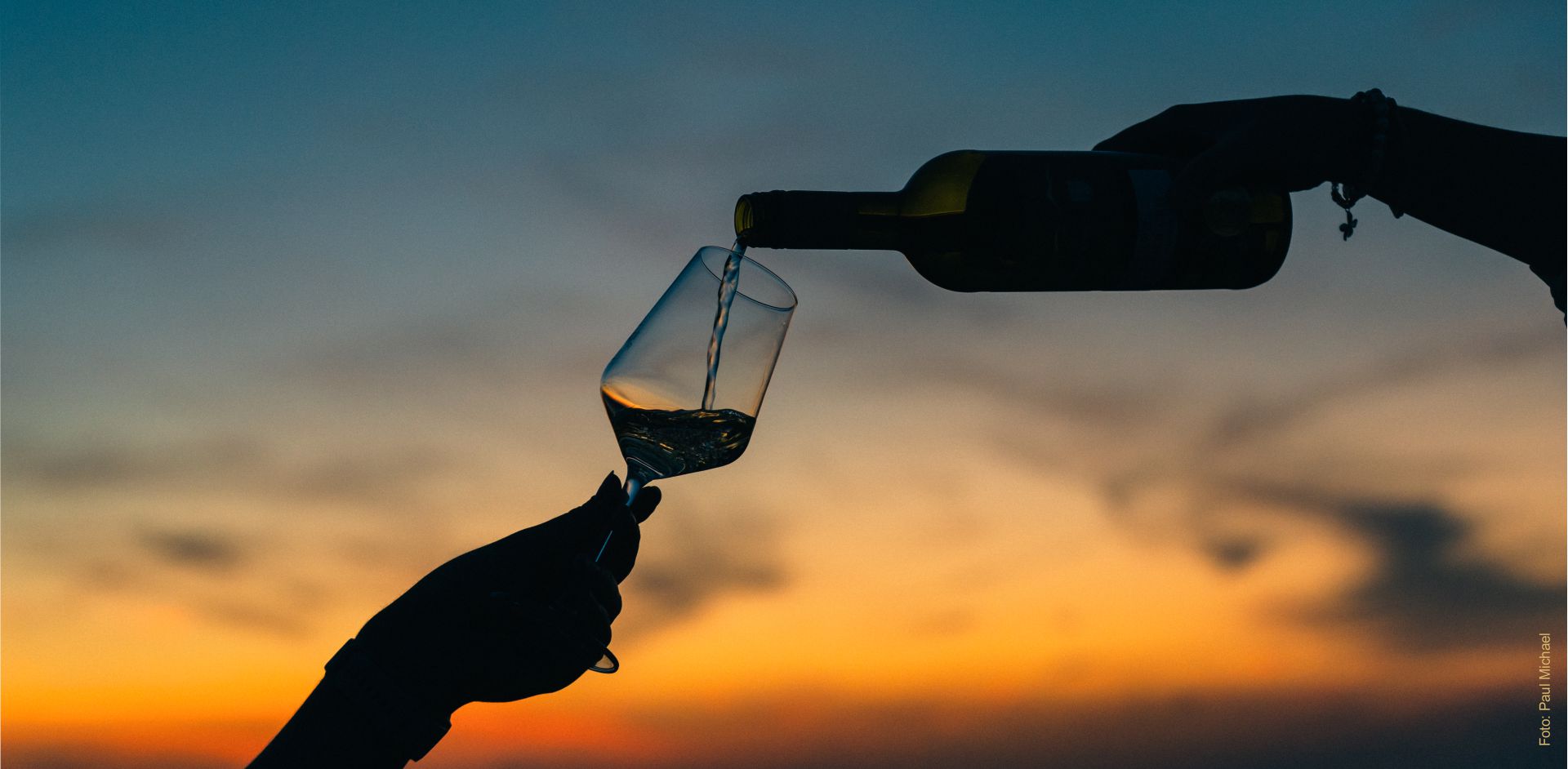 Ein Glas Wein wird eingeschenkt. Im Hintergrund ist das Abendrot bzw. der Sonnenuntergang zu sehen